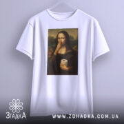 Футболка Мона мем, біла, підвішена на вішалці, фон світло-сірий, принт з Моною Лізою, яка тримає рулон туалетного паперу, вигляд спереду.