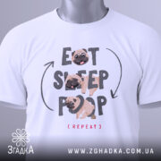 Футболка мопс ритуал, біла, складена на поверхні, фон світло-сірий, принт з текстом 'EAT SLEEP POOP (REPEAT)' та малюнками мопсів, на футболці є етикетка з зеленим шнурком.