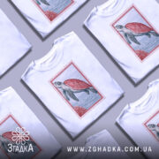 Футболка морська черепаха, біла, зображена на манекені, фон світло-сірий, принт з морською черепахою з червоною панцирем на фоні моря та коралів.