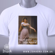 Футболка мотивуюча дівчина, біла, складена на поверхні, фон світлий, принт з дівчиною в традиційному вбранні, текст на українській мові: 'Чого тут думати? Треба робити!', на ярлику зелена стрічка.