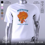 Футболка мовчання робить ягнят. Біла футболка з принтом, що зображає яскравого лева з відкритим ротом, на фоні світло-сірого. Принт має насичені кольори: оранжевий, зелений та блакитний, текст на українській мові. Ракурс фронтальний, футболка на манекені.