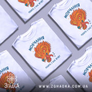 Футболка мовчання робить ягнят. Біла футболка з принтом, що зображає яскравого лева з відкритим ротом, на фоні світло-сірого. Принт має насичені кольори: оранжевий, зелений та блакитний, текст на українській мові. Ракурс фронтальний, футболка на манекені.