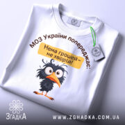 Футболка МОЗ України попереджає: складена біла футболка з принтом чорного птаха, текстом зверху та жовтою табличкою, на фоні світлого кольору.