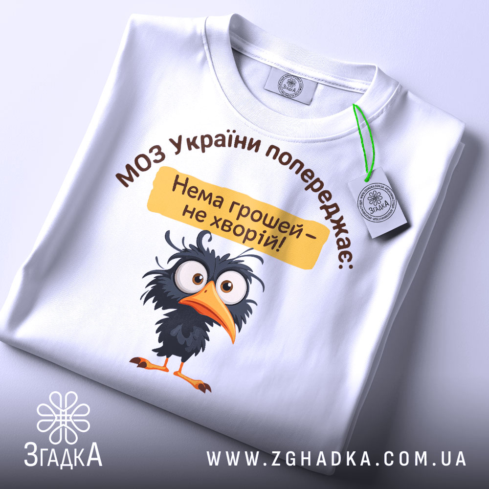 Футболка МОЗ України попереджає: складена біла футболка з принтом чорного птаха, текстом зверху та жовтою табличкою, на фоні світлого кольору.