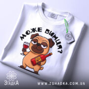 Футболка може винця білого кольору, складена на поверхні, фон світло-сірий, принт з мультяшним собакою, що тримає келих і пляшку, з етикеткою на комірці.