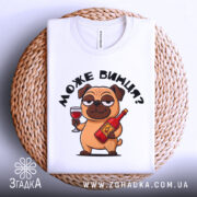 Футболка може винця білого кольору, складена на плетеній кошику, фон світло-сірий, принт з мультяшним собакою, що тримає келих і пляшку, з етикеткою на комірці.