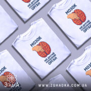 Футболка мозок другий орган. Біла футболка з принтом, на якому зображено червоний мозок та рука, що вказує на нього. Фон нейтральний, зображення з фронтального ракурсу. Текст на футболці чорного кольору.