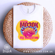 Футболка мозок під напругою, біла, складена на плетеній основі, фон світло-сірий, принт яскравий з зображенням мозку в руках, текст на принті помітний.