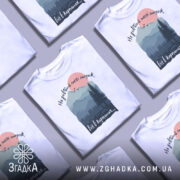 Футболка мозок в Карпатах, біла, зображена на манекені, фон нейтральний, принт з горами, лісом і сонцем, текст зверху: 'Не добивай метті мозок', внизу: 'віт в карпатах...'.