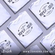 Футболка мрій дій, білого кольору, зображена на манекені, фон світло-сірий, принт чорного кольору з написом 'МРІЙ-ДІЙ' та декоративними елементами.