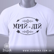 Футболка мрій дій, білого кольору, складена на поверхні, фон світло-сірий, принт чорного кольору з написом 'МРІЙ-ДІЙ' та етикетка з зеленим шнурком.