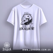 Футболка мрій і досліджуй, біла, підвішена на вішалці, фон світлий, принт з космічним кораблем та місяцем, текст 'Досліджуй!' внизу.