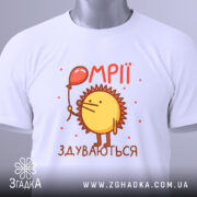 Футболка мрії здуваються, біла, зображена зверху, фон світло-сірий, принт з жовтим сонечком, що тримає червоний повітряний шар, текст 'ОМПІІ ЗДУВАЮТЬСЯ' у червоному кольорі, з етикеткою на комірці.