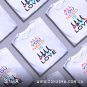 Футболка музика серця. Біла футболка з коротким рукавом, зображена на манекені, фон світло-сірий. Принт містить текст 'ALL YOU NEED IS LOVE' у різних кольорах, а також силуети людей, що йдуть, на кольорових трикутниках.