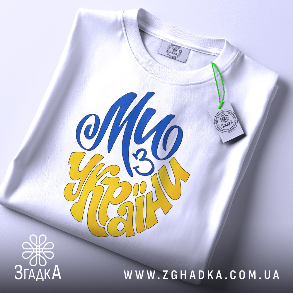 Футболка ми з України білого кольору, зображена зверху, складена на поверхні, фон світло-сірий, принт у синьому та жовтому кольорах, напис "Ми з України" розташований по центру, на футболці є етикетка з зеленим шнурком.