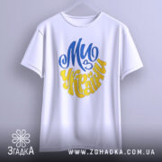 Футболка ми з України білого кольору, зображена з фронтального ракурсу на вішалці, фон світло-сірий, принт у синьому та жовтому кольорах, напис "Ми з України" розташований по центру.