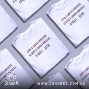 Футболка Миколай дітям. Білий колір, зображена з фронтального ракурсу на манекені. Фон світло-сірий, принт містить текст з червоними закресленнями та чорним написом 'Привіт, діти!'.