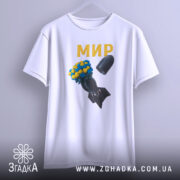 Футболка мир без війни, біла, підвішена на вішалці, фон світло-сірий, принт з квітами жовтого та синього кольору на чорній бомбі, текст 'МИР' золотистого кольору.