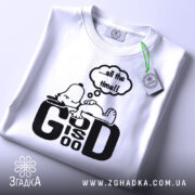 Футболка мир серце біла, зображена на столі, фон світло-сірий, принт чорний з персонажем, що лежить, та текстом '...all the time!!', з етикеткою зеленого кольору.