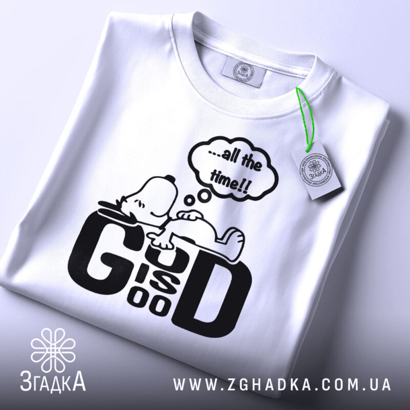 Футболка мир серце біла, зображена на столі, фон світло-сірий, принт чорний з персонажем, що лежить, та текстом '...all the time!!', з етикеткою зеленого кольору.