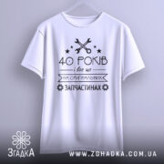 Футболка на оригінальних запчастинах, білого кольору, підвішена на вішалці, фон світло-сірий, принт чорного кольору з текстом "40 РОКІВ і все це на ОРИГІНАЛЬНИХ ЗАПЧАСТИНАХ" та зображенням ключів і зірочок.
