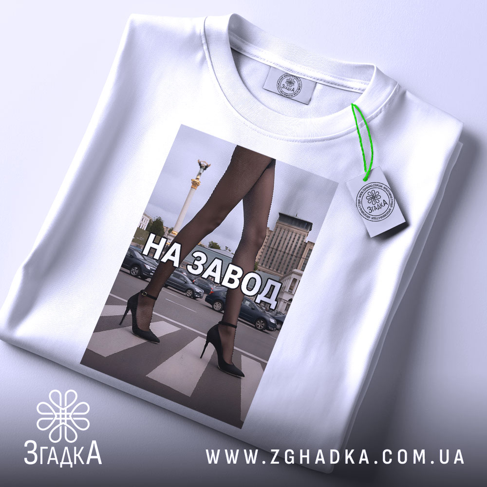 Футболка на завод, біла, зображена з верхнього ракурсу, фон світлий, принт з зображенням жіночих ніг у чорних колготках та туфлях на високих підборах, текст "НА ЗАВОД" великими літерами, на комірці видна етикетка.