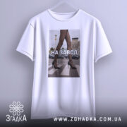 Футболка на завод, біла, зображена з бокового ракурсу, фон нейтральний, принт з зображенням жіночих ніг у чорних колготках та туфлях на високих підборах, текст "НА ЗАВОД" великими літерами, футболка підвішена на вішалці.