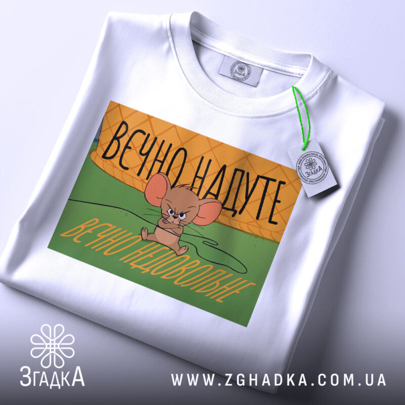 Футболка надуте недовольне, біла, зображена з верхнього ракурсу, фон нейтральний, принт з малюнком мишеняти, яке виглядає незадоволено, текст на принті українською мовою: 'ВЕЧНО НАДУТЕ ВЕЧНО НЕДОВОЛЬНЕ', на футболці є етикетка з зеленим шнурком.