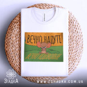 Футболка надуте недовольне, біла, зображена зверху на плетеному фоні, принт з малюнком мишеняти, яке виглядає незадоволено, текст на принті українською мовою: 'ВЕЧНО НАДУТЕ ВЕЧНО НЕДОВОЛЬНЕ'.