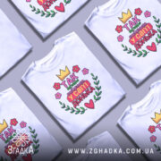 Футболка найкраща донька, біла, зображена на манекені, фон світло-сірий, принт з короною, квітами та написом 'Так виглядає найкраща у світі донька'.