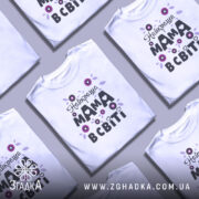 Футболка найкраща мама, білого кольору, зображена з фронтального ракурсу на манекені, фон світло-сірий, принт з квітами та написом "Найкраща мама в світі" в чорному та фіолетовому кольорах.