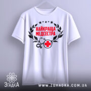 Футболка найкраща медсестра, білого кольору, зображена з фронтального ракурсу на вішалці, фон світло-сірий, принт містить червоний текст "НАЙКРАЩА МЕДСЕСТРА" з чорними елементами у вигляді стетоскопа та червоного хрестика.