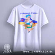 Футболка найкраща сваха, біла, підвішена на вішалці, фон світлий, принт з дівчиною в українському вбранні, яка тримає качалку і кошик з солодощами, на фоні контур України з жовто-синім кольорами.