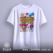 Футболка найкраща внучка, біла, зображена з фронтального ракурсу, підвішена на вішалці, фон світло-сірий, принт кольоровий з малюнком дівчинки, зірочками, серцями та квітами.