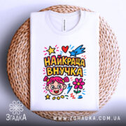 Футболка найкраща внучка, біла, зображена зверху, складена на плетеній основі, фон білий, принт кольоровий з малюнком дівчинки, зірочками, серцями та квітами.