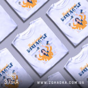 Футболка найкращий бухгалтер, біла, зображена з правого ракурсу, фон нейтральний, принт з жінкою в жовтій блузці, яка тримає різні документи та гаджети.