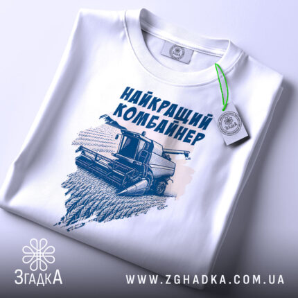 Футболка найкращий комбайнер, білого кольору, зображена в складеному вигляді на поверхні, фон світло-сірий, принт з комбайном та написом виконаний у темно-синьому кольорі, на футболці є етикетка з зеленим шнурком.