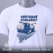 Футболка найкращий комбайнер, білого кольору, зображена в складеному вигляді на поверхні, фон світло-сірий, принт з комбайном та написом виконаний у темно-синьому кольорі, на футболці є етикетка з зеленим шнурком.