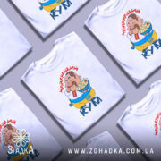 Футболка найкращий кум, біла, зображена на манекені з правого боку, фон градієнтний сірий, принт з веселим персонажем, який тримає тарілку з їжею, текст "НАЙКРАЩИЙ КУМ" червоним шрифтом.