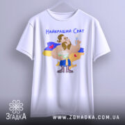 Футболка найкращий сват, білого кольору, підвішена на вішалці, фон нейтральний, принт з мультяшним персонажем, що тримає тарілку з варениками, на фоні жовто-блакитний прапор України, текст "Найкращий Сват" зверху.