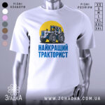 Футболка найкращий тракторист. Біла футболка з коротким рукавом, зображення трактора на жовтому фоні, текст 'НАЙКРАЩИЙ ТРАКТОРИСТ' синього кольору під принтом, фон нейтральний, футболка представлена на манекені.