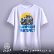 Футболка найкращий тракторист. Біла футболка з коротким рукавом, зображення трактора на жовтому фоні, текст 'НАЙКРАЩИЙ ТРАКТОРИСТ' синього кольору під принтом, футболка підвішена на вішалці, фон світлий.