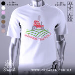 Футболка найкращий тракторист. Біла футболка з коротким рукавом, зображена з фронтального ракурсу на манекені. На фоні світло-сірий колір. Принт містить червоний трактор, що курить, на зелених полях, з написом 'найкращий тракторист' у червоному кольорі.