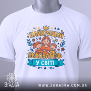 Футболка найкращий вихователь, білого кольору, зображена зверху, на фоні світло-сірого кольору, принт з малюнком жінки з двома дітьми та написом 'НАЙКРАЩИЙ ВИХОВАТЕЛЬ У СВІТІ', на футболці є етикетка з зеленим шнурком.