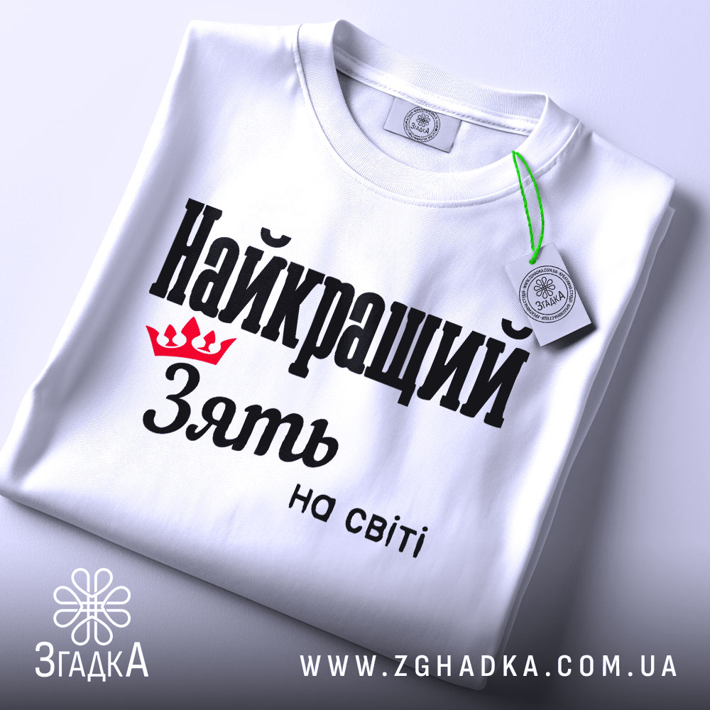 Футболка найкращий зять, біла, складена на поверхні, фон світло-сірий, принт чорного кольору з червоною короною та текстом 'Найкращий зять на світі', з етикеткою на шнурку.