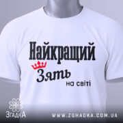 Футболка найкращий зять, біла, складена на поверхні, фон світло-сірий, принт чорного кольору з червоною короною та текстом 'Найкращий зять на світі', з етикеткою на шнурку.