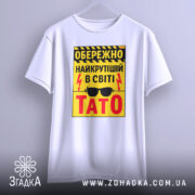Футболка найкрутіший тато, біла, зображена на вішалці, фон світло-сірий, принт жовтий з чорними і червоними елементами, текст з попередженням і написом 'ТАТО'.