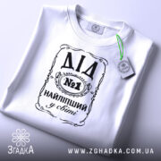 Футболка найліпший дід, білого кольору, зображена зверху на плоскій поверхні, фон світло-сірий, принт чорного кольору з написом 'ДІД №1 НАЙЛІПШИЙ у світі', на футболці є етикетка з зеленим шнурком.