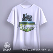 Футболка найліпший тракторист. Біла футболка з коротким рукавом, підвішена на вішалці. На фоні світло-сірий колір. Принт з трактором та написом 'НАЙЛІПШИЙ ТРАКТОРИСТ' у зелених та чорних тонах.