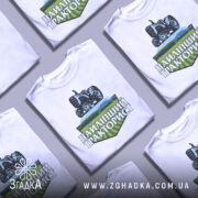 Футболка найліпший тракторист. Біла футболка з коротким рукавом, зображена на манекені з металевим блиском. На фоні світло-сірий колір. Принт з трактором та написом 'НАЙЛІПШИЙ ТРАКТОРИСТ' у зелених та чорних тонах.